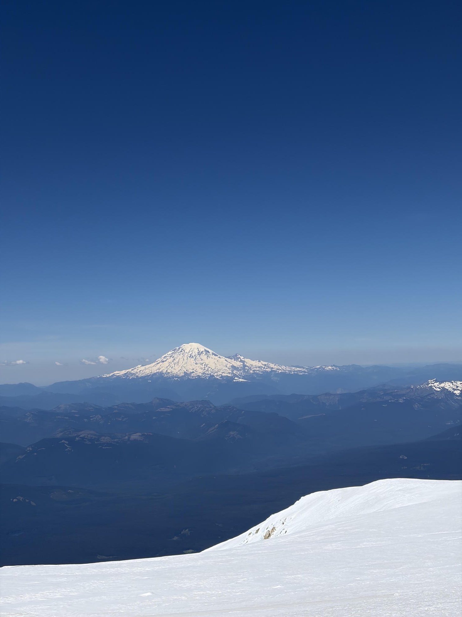 Snowfield in the foreground with Mt. Rainier floating on the horizon across a sea of ridges