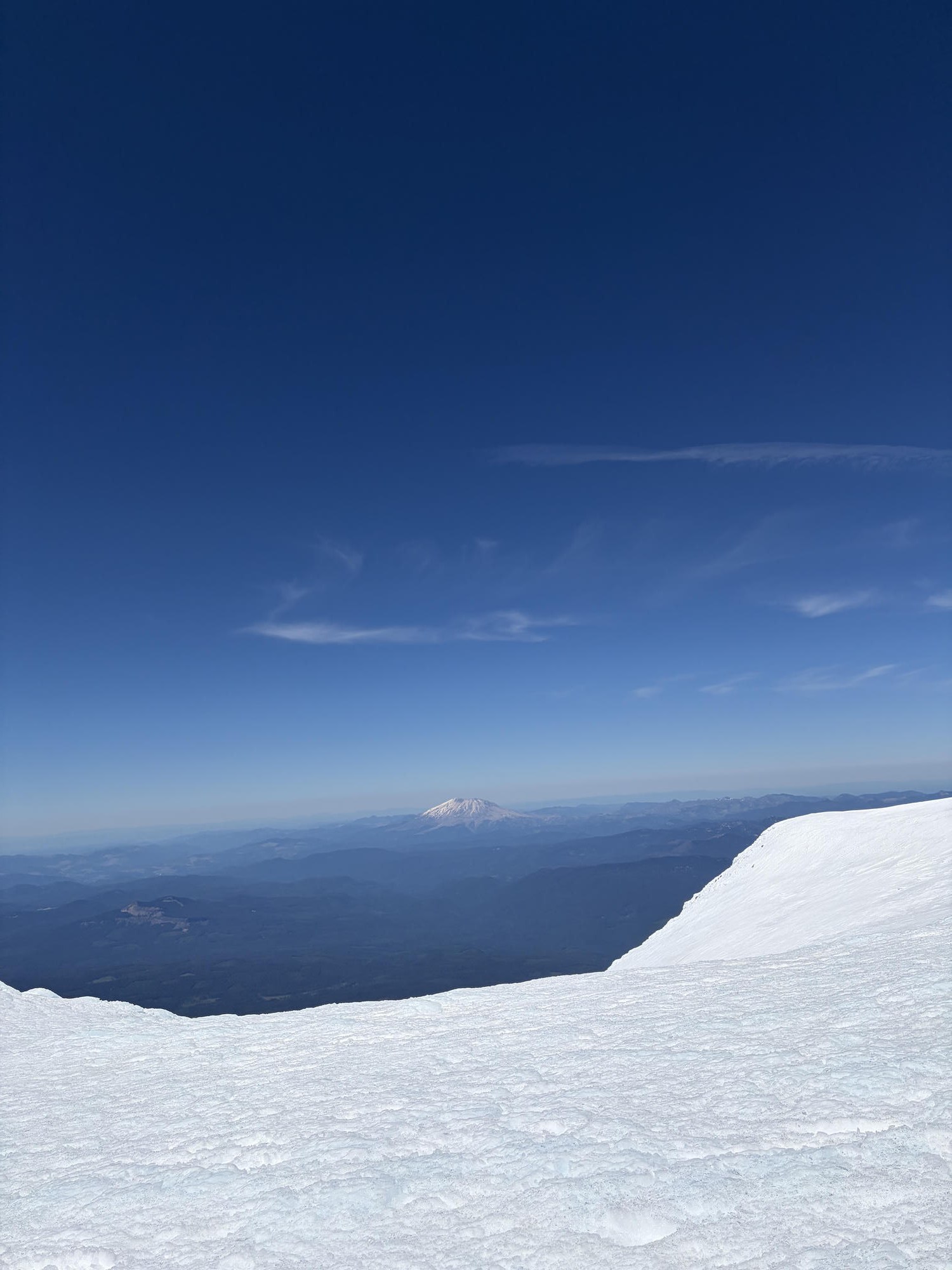 Wide summit view over the snow with Mt. St. Helens in the distance under clear skies