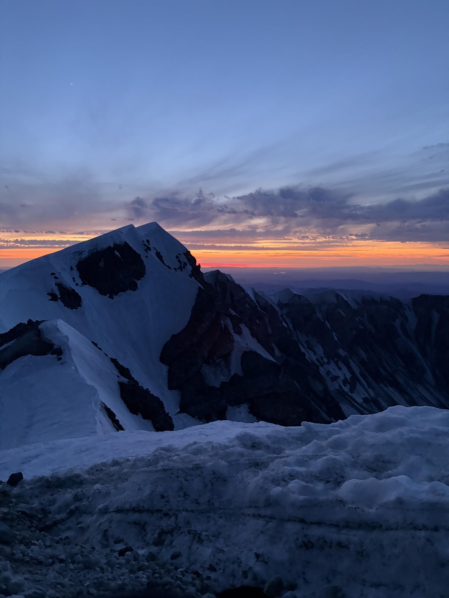 Alpenglow sunset over the snowy crater rim and distant ridgelines from near the summit