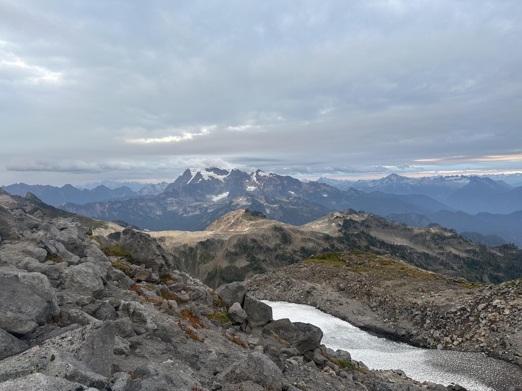 Rocky ridge foreground with a snow-filled tarn and Mount Shuksan across the valley