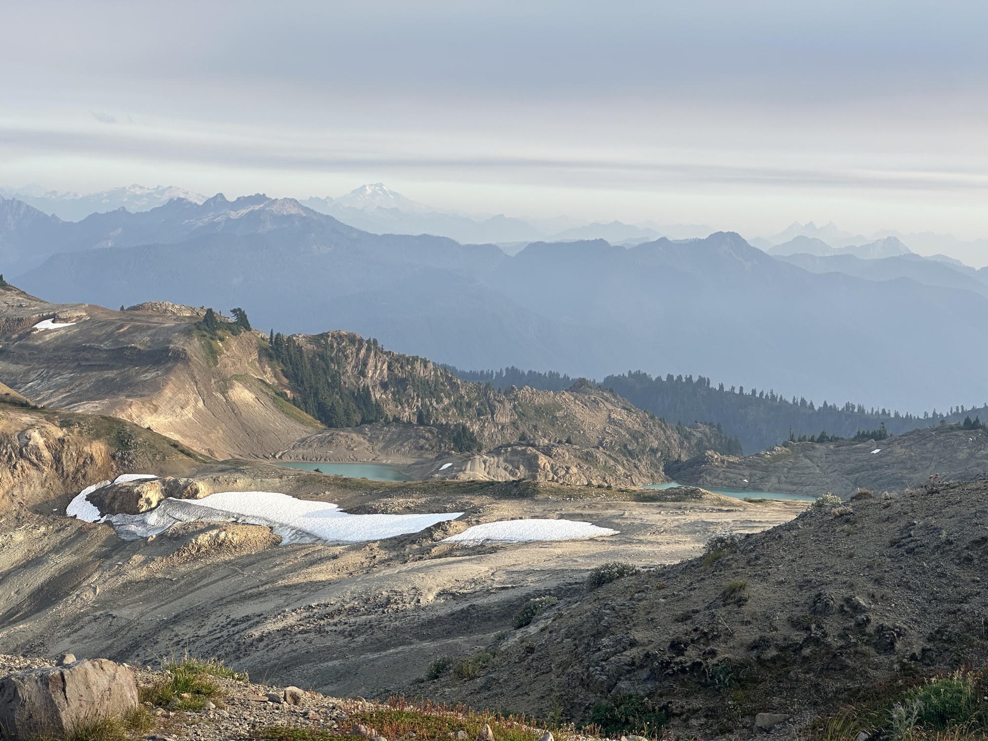 Turquoise alpine tarns and lingering snowfields on Ptarmigan Ridge with hazy peaks beyond